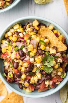 two bowls filled with black beans, corn and cilantro salsa next to tortilla chips