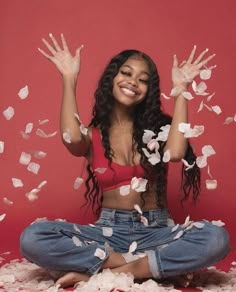 a woman sitting on the floor with her hands in the air and petals flying around her