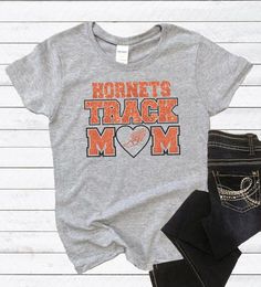 Track Mom T-Shirt, Track and Field, Track Mom Tee, Track Mom Gift, Sports Mom T-Shirt Athletic Heather Cotton T-shirt For Fans, Athletic Heather Graphic Cotton T-shirt, Athletic Heather T-shirt With Letter Print For Sports, Athletic Heather Fan Apparel T-shirt For Sports Season, Pre-shrunk Heather Grey T-shirt For Fan Merchandise, Athletic Heather T-shirt For Sports Season, Cotton T-shirt In Athletic Heather With Letter Print, Pre-shrunk Athletic Heather T-shirt For Game Day, Athletic Heather Short Sleeve Fan Merchandise T-shirt