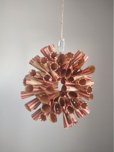 an ornament made out of brown paper tubes hanging from a string on a gray wall