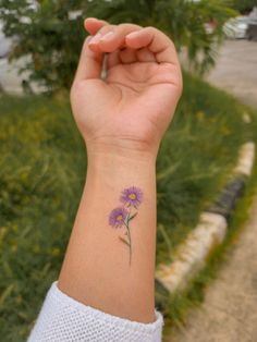 a woman's wrist with a purple flower tattoo on the left side of her arm