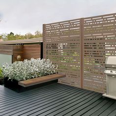 an outdoor kitchen with grill and planters on the outside deck area, next to a wooden fence