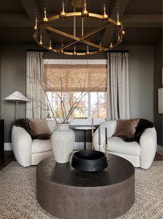 a living room with two white couches and a round coffee table in front of a window