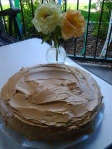 a frosted cake sitting on top of a table next to a vase with flowers