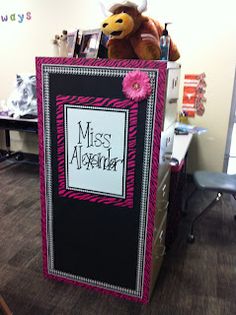 a stuffed animal sitting on top of a blackboard in an office cubicle with pink accents