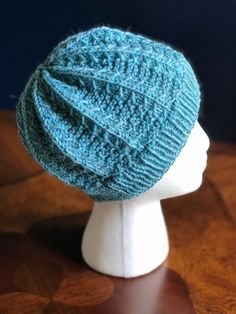 a white mannequin head wearing a blue knitted hat on top of a wooden table