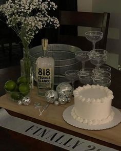 a table topped with a white cake and lots of glasses next to a bottle of booze