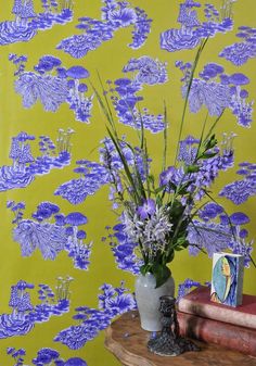 a vase filled with purple flowers sitting on top of a table next to a book