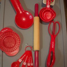 red kitchen utensils are laid out on a gray tray with scissors, measuring spoons and spatulas