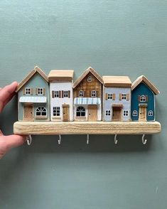 a hand holding a wooden shelf with three houses on it and two hooks attached to the wall