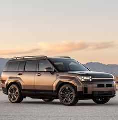 an suv is parked on the road in front of some mountains and hills at sunset