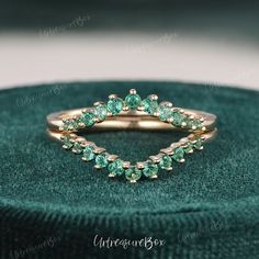 a gold ring with green stones in it sitting on top of a velvet cushioned box