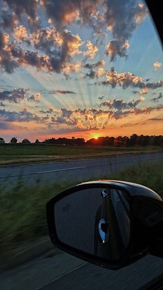 the sun is setting in the distance as seen from a car's side view mirror