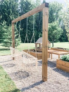 a wooden swing set in the middle of a graveled area next to some trees