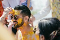 a man with yellow paint on his face and chest is surrounded by other people in the background