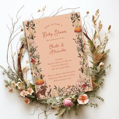 an orange and pink baby shower with flowers on the bottom is surrounded by greenery