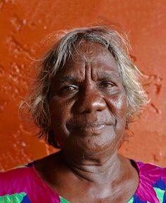 an older woman standing in front of a red wall with her eyes open and looking at the camera