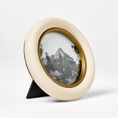 a white and gold photo frame with mountains in the background, on a black stand