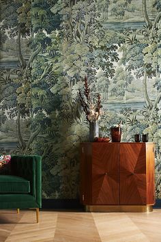 a green chair sitting next to a wooden cabinet in front of a wall with trees on it