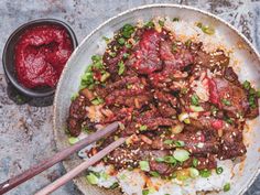 meat and rice in a bowl with chopsticks on the side