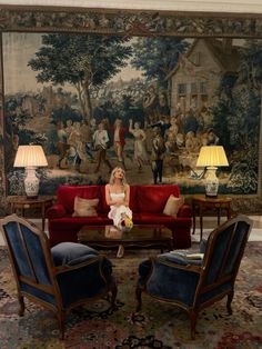 a woman sitting on top of a red couch in front of a wall mural with people