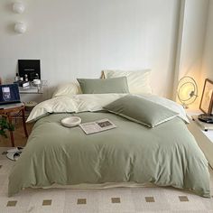 a bed in a bedroom with green sheets and pillows on top of it, next to a laptop computer