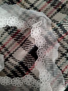 white lace is laying on top of a plaid fabric with black and red stripes in the background