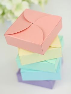 there is a small pink box sitting on top of many other colored boxes in front of a white flower