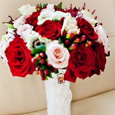 a white vase filled with red and pink flowers on top of a table next to a couch