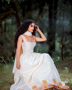 a woman in a white dress is sitting on a tree stump and posing for the camera