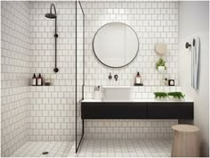 a bathroom with white tiles and black counter tops, along with a round mirror on the wall