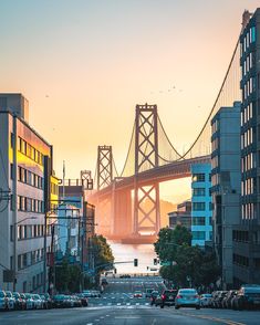 cars are driving on the road near tall buildings and a bridge in the background at sunset