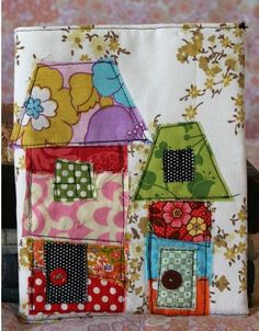 a close up of a small patchwork bag with houses on it and flowers in the background