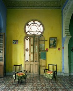 two chairs sitting in front of a doorway with a clock on the wall above it