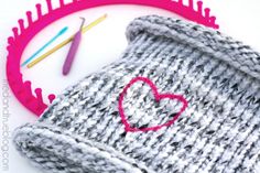 a knitted hat with a heart on it next to crochet needles and scissors