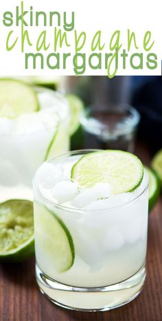 two glasses filled with ice and limes next to each other on a wooden table