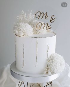 a white wedding cake with gold lettering and pom - poms on the top