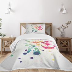 a bed covered in a white comforter with colorful paint splatters on it