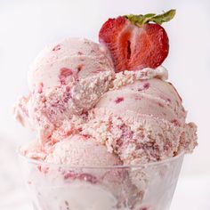 two scoops of strawberry ice cream in a glass bowl with a strawberries on top