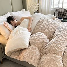 a woman laying on top of a bed covered in blankets and pillows next to a night stand