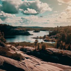 a lake surrounded by rocks and trees on a sunny day with clouds in the sky