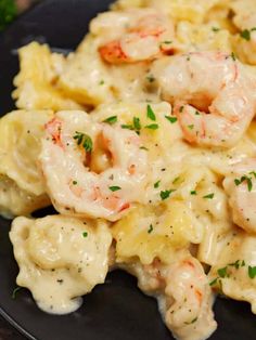 pasta with shrimp and cream sauce on a black plate, garnished with parsley