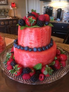 a watermelon cake with berries and mints on top sits on a glass plate