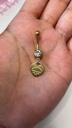 a person is holding a gold heart shaped belly ring with a diamond in the middle