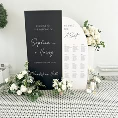 a black and white wedding ceremony sign with flowers on the floor next to an arch