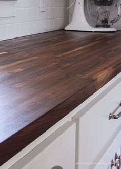 a kitchen counter top with a mixer on the wall in the back ground and white cabinets to the side