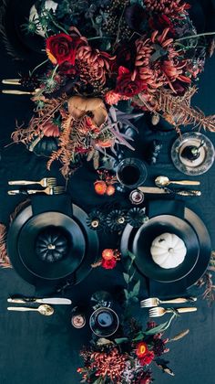 the table is set with black plates, silverware and floral centerpieces on it