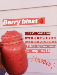 a person holding up a strawberry banana smoothie in front of a sign that says berry blast