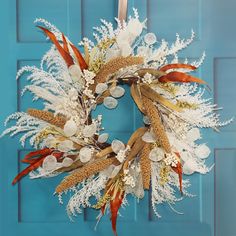 a wreath is hanging on a blue door with white and red flowers, feathers and coins