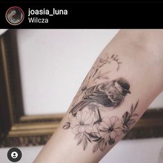 a bird sitting on top of a branch with flowers around it's neck and arm